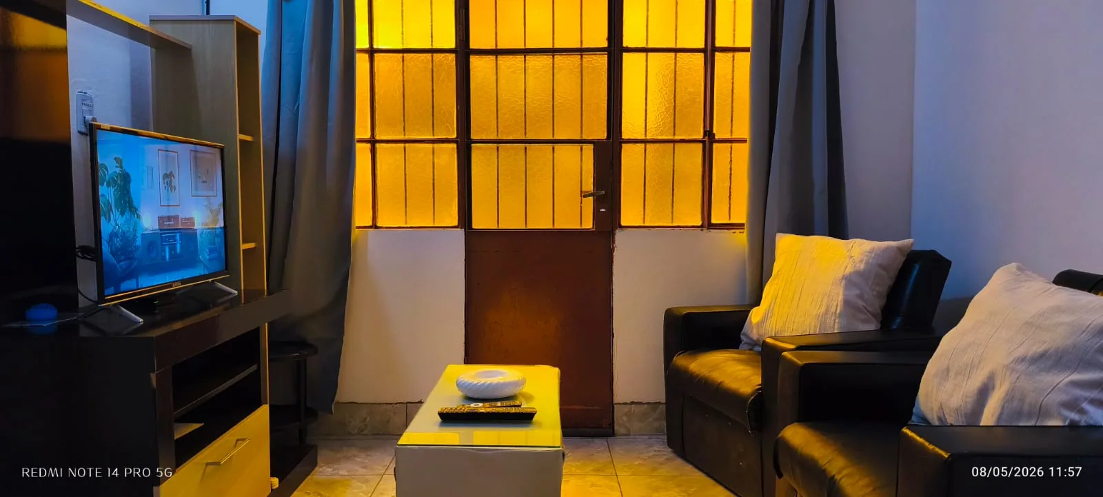 Living con dos sillones, mesa baja y televisor junto a una puerta con vidrios de color ámbar.